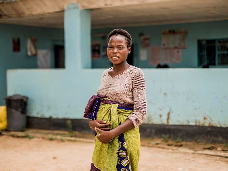 Kiera standing outside building, looking at camera and holding stomach.