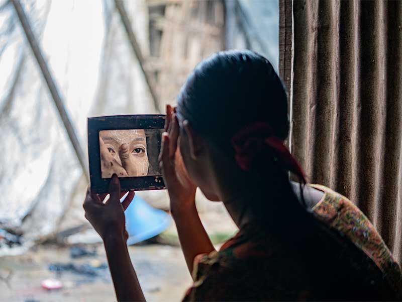 Useaking using mirror to apply thanaka paste to her face.