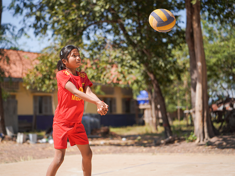 11 year old girl in red sports t-shirt and shorts hitting volleyball outside