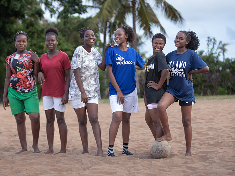 Group of women standing on sand with a football smiling at camera