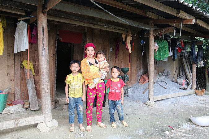 Dia with her children standing outside their home in Vietnam