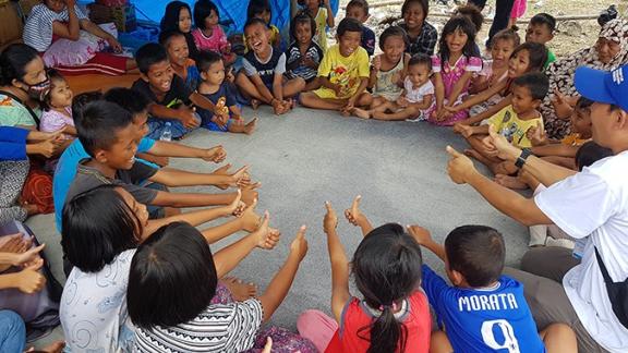 A Plan International staff member leads games in a child friendly space, following the 2018 Indonesia earthquake