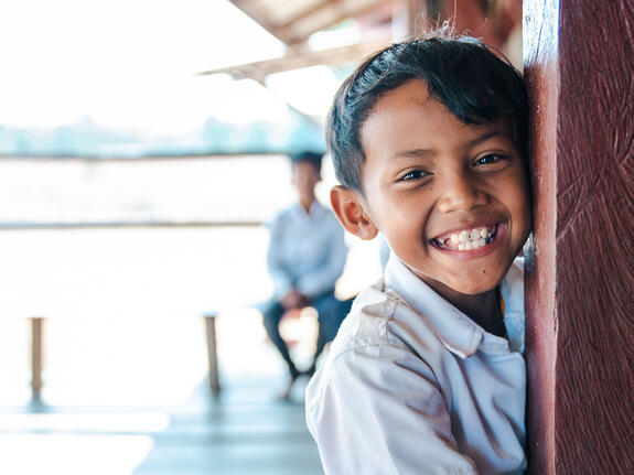 Young boy in white shirt leaning against post and smiling at camera