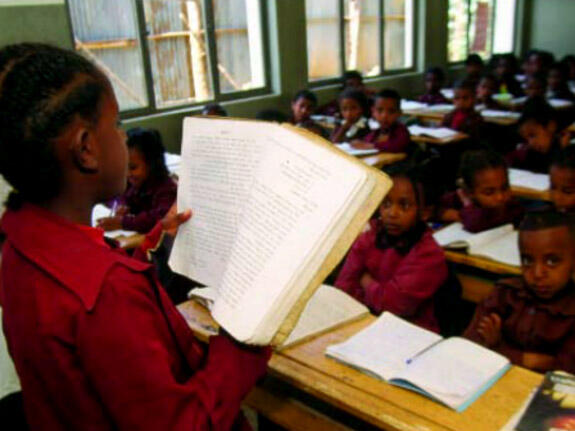 A pupil reads from a book to a classroom of students