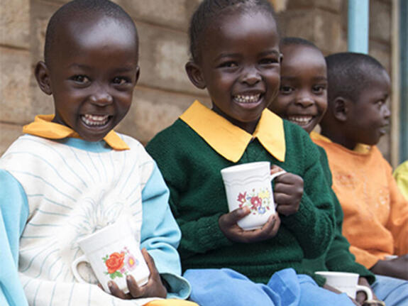 Four young children in Kenya smiling and drinking from mugs