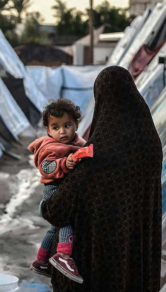 A Palestinian woman holding her child in a refugee camp