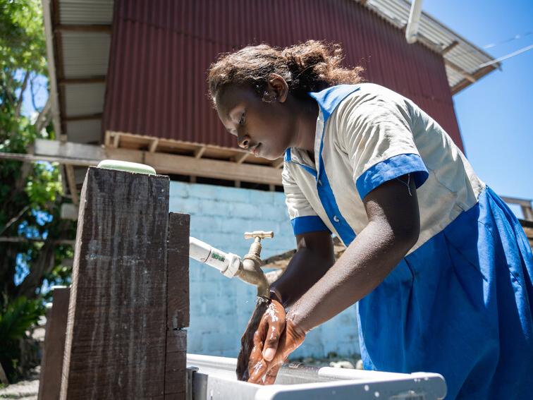 Evita washes her hands in handwashing station that includes tap and sink