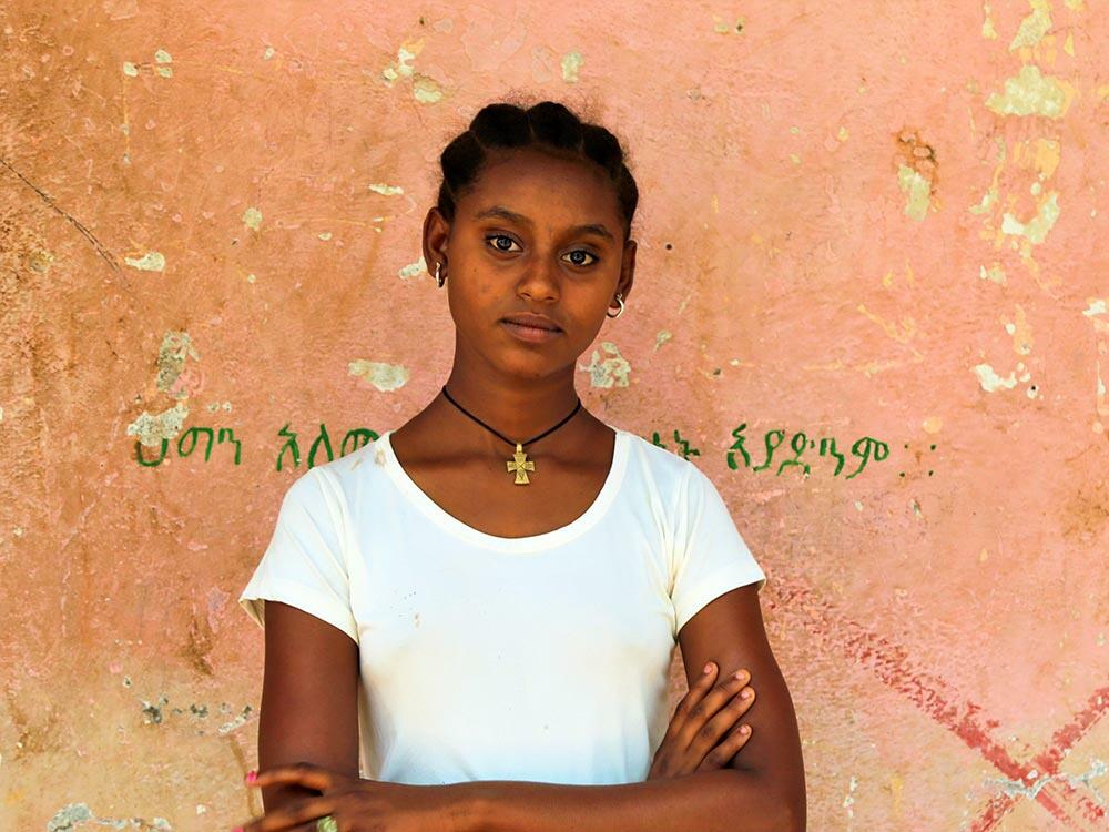 Worke, 14, standing with arms crossed in front of a wall looking at the camera