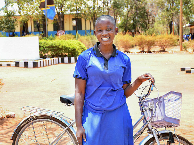 Anitha standing with her bike outside, smiling at camera