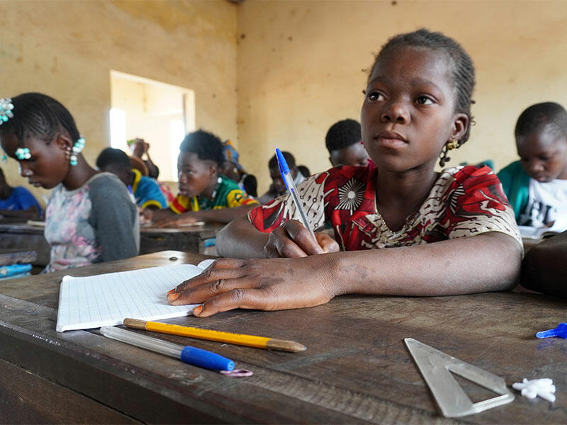 Diatou at school desk taking notes with other pupils also working in background. 