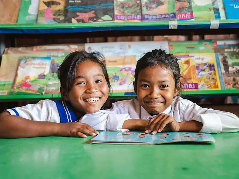 Len Sokha and her school friend sat in school library with open book smiling at camera
